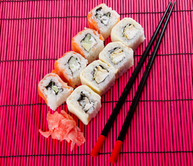 Sushi rolls, ginger and chopsticks (on a bright red bamboo background)