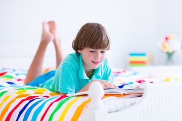 School boy reading a book in bed