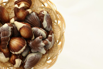 chocolate candy shaped sea shells in a wicker basket on the white background