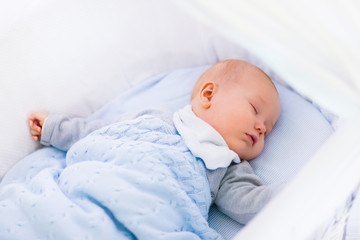 Baby boy in a crib under knitted blanket