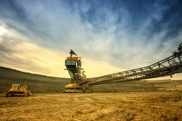 Fototapeta premium One side of huge mining drill machine and dredger photographed from a ground with wide angle lens. Dramatic and colorful sky in background.