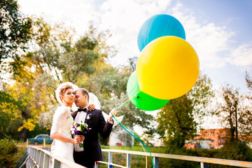 Жених и невеста обнимаются на мосту с воздушными шарами на фоне осеннего пейзажа © meatbull