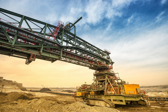 One side of huge coal mining drill machine photographed from a ground with wide angle lens. Dramatic and colorful sky in background.