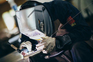 Manual worker doing his hard job using welding mask, tools and machinery on metal. Selective focus...