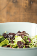 mixed leaf salad in a blue bowl with wooden background