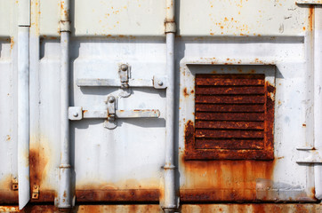 Fragment of a door of old sea shipping container. Rusty ventilation grille and flaking white paint.