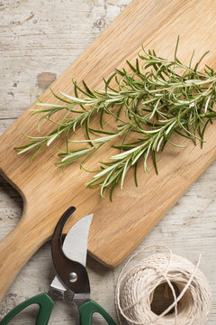 Chopping board with rosemary lying on top of a worn wooden surfa