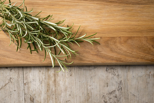 Rosemary on a chopping board  lying on top of an aged wooden sur