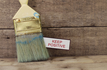 cropped image concept, used paint brush and white card with word KEEP POSITIVE printed on it.wooden...
