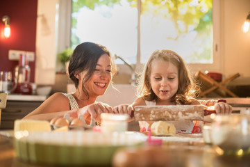 A mother and her daughter are working a pastry with a rolling pin