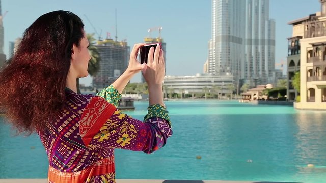 Pretty woman stands near the blue pool and makes photos on his smartphone. Female makes photos on his smartphone. Businesswoman with smartphone. Adult woman uses smartphone