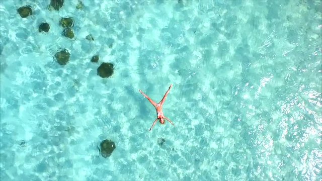AERIAL SLOW MOTION: Beautiful young woman swimming, lying on a water surface in crystal clear ocean