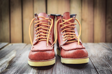 A pair of brown leather boots with laces placed on wooden floor, selective focus
