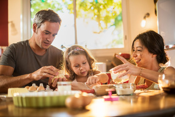 A four years old blonde girl is cooking cakes with parents