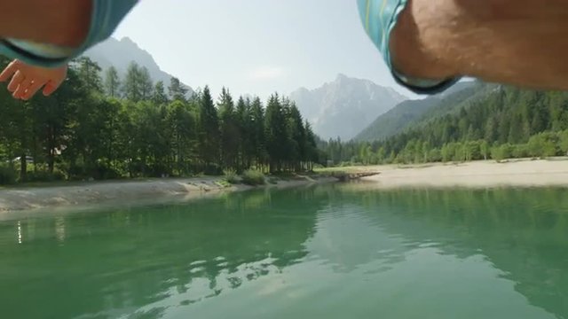 SLOW MOTION: Young man in swimsuit jumping and diving into the beautiful mountain lake in sunny summer