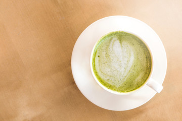 A cup of green tea matcha latte with saucer. Wood table background. Top view.