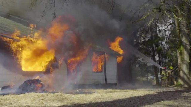 Firefighters hose down huge flames coming from a burning house 