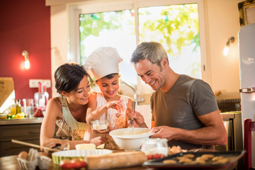 Happy 7 years old girl with chef hat is cooking with her parents