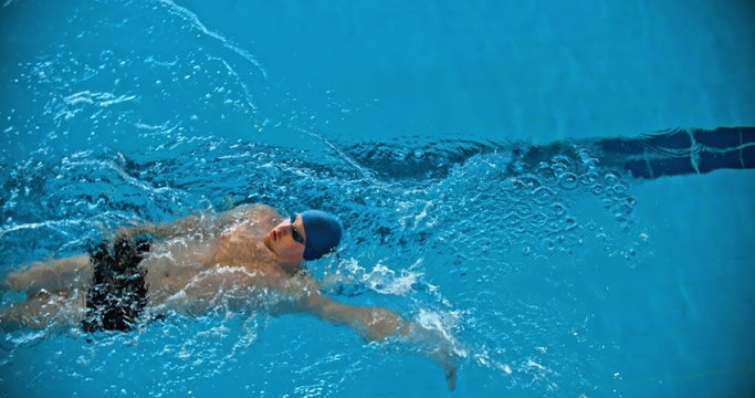 Directly above view of man in goggles and cap swimming backstroke in the pool