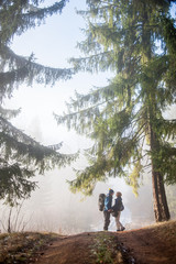 Traveler couple in love enjoying thier hike in foggy autumn day on the mountain forest path. Side view of man and woman holding hands.