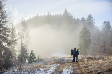 young couple of tourists staying in the winter woods on the road and look at each other, Carpathians Ukraine
