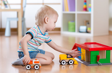 Little blond toddler kid boy plays with toy car