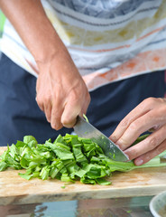 Man cutting green salad on the wooden board