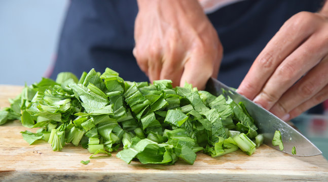 Man cutting green salad on the wooden board