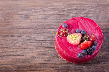 Delicious raspberry cake with fresh strawberries, raspberries, blueberry, currants and pistachios on wooden background. free space for your text.