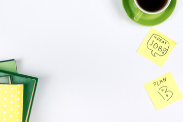 Office table desk with green supplies, blank note pad, cup, pen, glasses, crumpled paper, magnifying glass, flower on white background. Top view