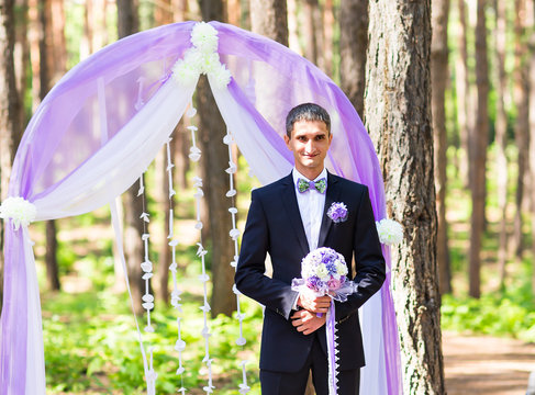 rich stylish groom with bridal bouquet waiting bride near the wedding arch 