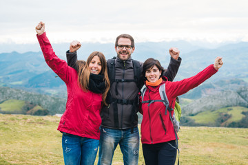three young smiling friends hiking outside embracing and doing success fists up sign. Outdoor healhy happy lifestyle.
