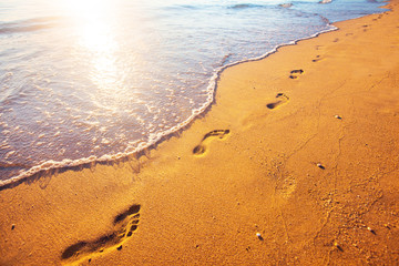 beach, wave and footprints at sunset time