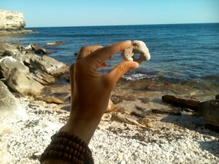 Камень с дырочкой в руке на фоне моря летний отпуск