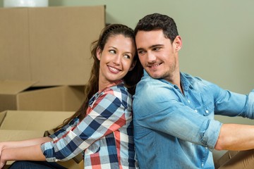 Young couple sitting back to back in their new house