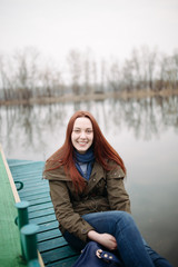 Woman sitting on pier at the river in a cold cloudy day and smile