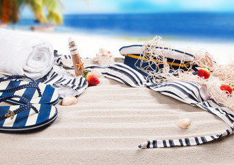 Marine sandal, flip- flop, swimsuit and summer accessories on sand with tropical beach background