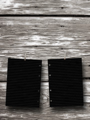 Close-up of two hanged black blank frames with pegs against weathered wooden background