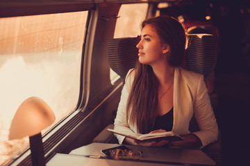 young girl travels on a high-speed comfortable train that runs on a tablet and answer the messages on the phone, surfing on the Internet, outdoor portrait, fashion model, close up