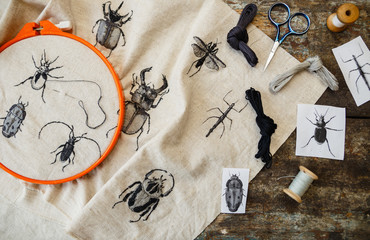Embroidery in process with hoop and sewing threads on table. Embroidered beetles.