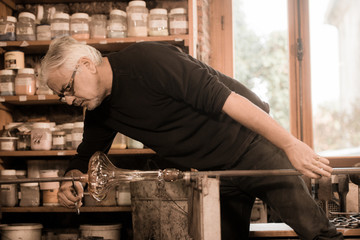 Glassblower forming molten glass in his worshop