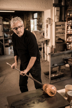 Glassblower forming molten glass in his worshop