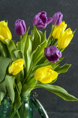 Naklejka premium Yellow and violet tulips in the jar. Grey background. Spring, easter.
