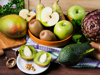 Fresh green fruit and vegetables on wooden table - apples, kiwi, pears, mango, avocado and artichokes