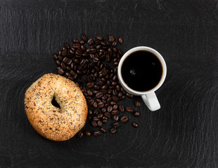 Dark coffee and bagel with roasted beans on natural slate stone
