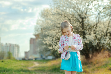 Naklejka premium Beautiful happy little girl enjoying smell in a flowering sprin