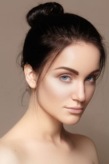 Beautiful young woman with clean face, shiny skin, fashion natural make-up, perfection eyebrows. Cute bun hairstyle. Spa portrait, naturel cosmetics, healthy fresh look


