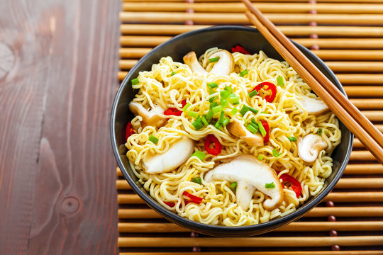 Instant noodles with shiitake mushrooms, pepper and onion in a bowl, Asian meal on a table, top view