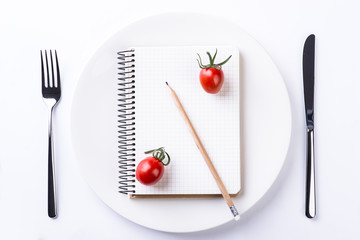 Plate, fork, knife, tomatoes, pencil and notebook tape on wooden