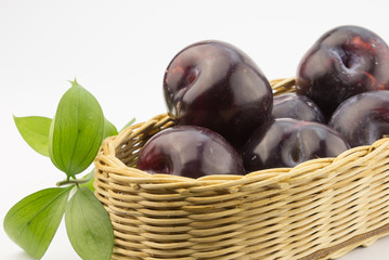 Close up photo of dark plums in a basket on white